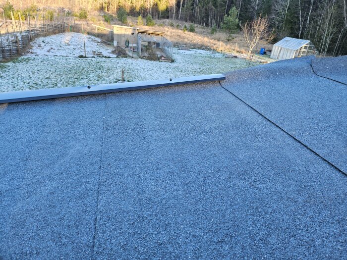Takpapp lagt på tak med snöklädd bakgrund och några träd. Vindskivor på plats, förberedelse för skorsten pågår.