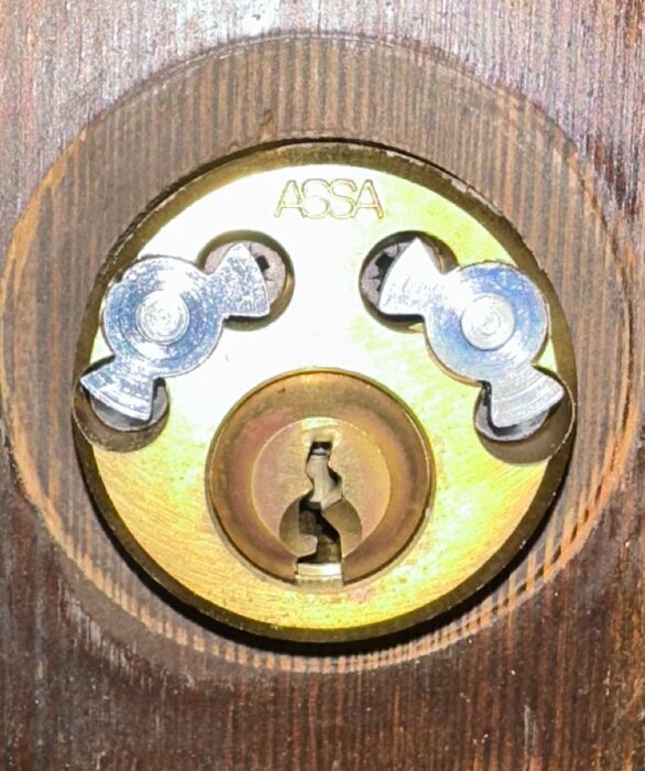 En närbild av ett ASSA-lås infällt i en träyta.