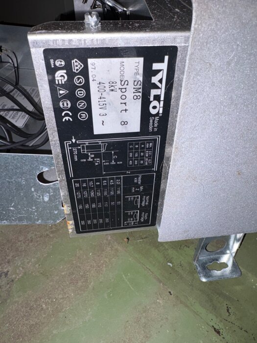 Tylö SM8 Sport 8 bastuaggregat, 8kW, placerat på grönt betonggolv, visar teknisk specifikation på en etikett.