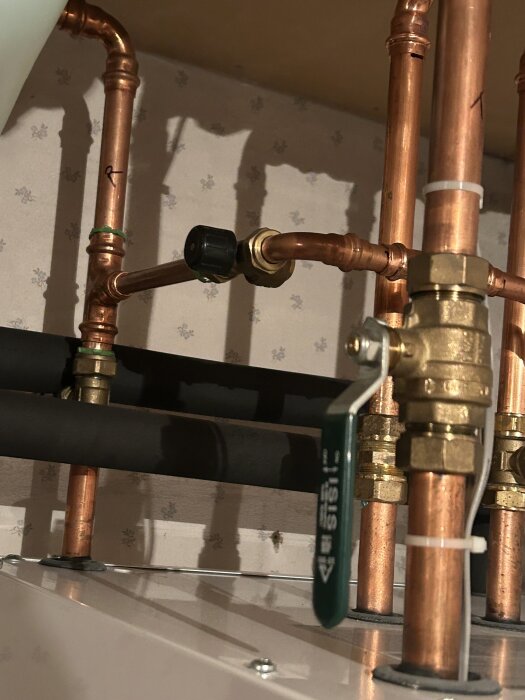 Närbild av en ventil på ett kopparrör märkt "R" och kopplat till inkommande vattenrör som fortsätter till en pump.