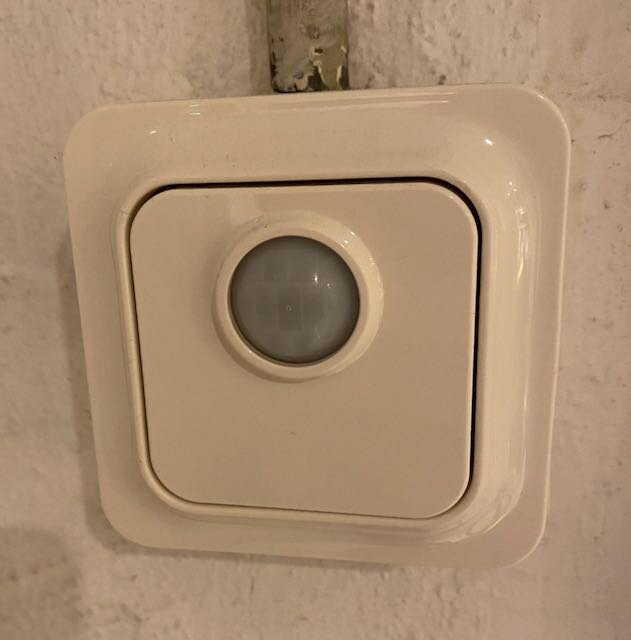 En vit rörelsevakt monterad på en vägg, använd för att styra tak-spotar med LED-lampor.