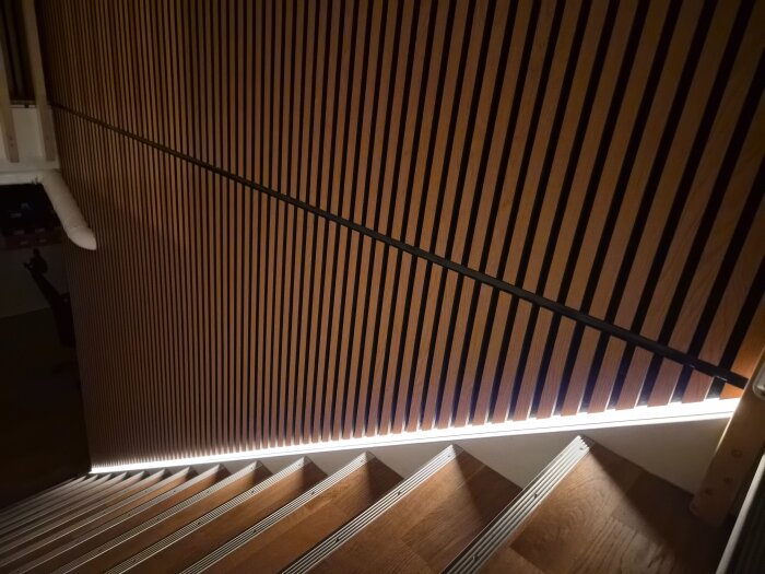 Svart aluminiumprofil med mörktonat lock och LED-strip på en trävägg vid trappa, visar skarvlösning; en LED igång för jämförelse.
