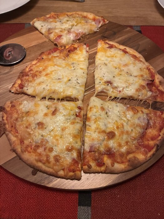 Hemlagad pizza med cheddar- och mozzarellaost på en träbricka, delvis skuren i bitar.