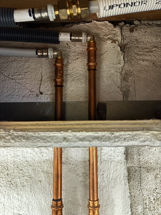 Rörinstallation med kopparrör och plastslang i en betongvägg, förberedelse för att sätta in kulventiler och dra rör genom väggen.