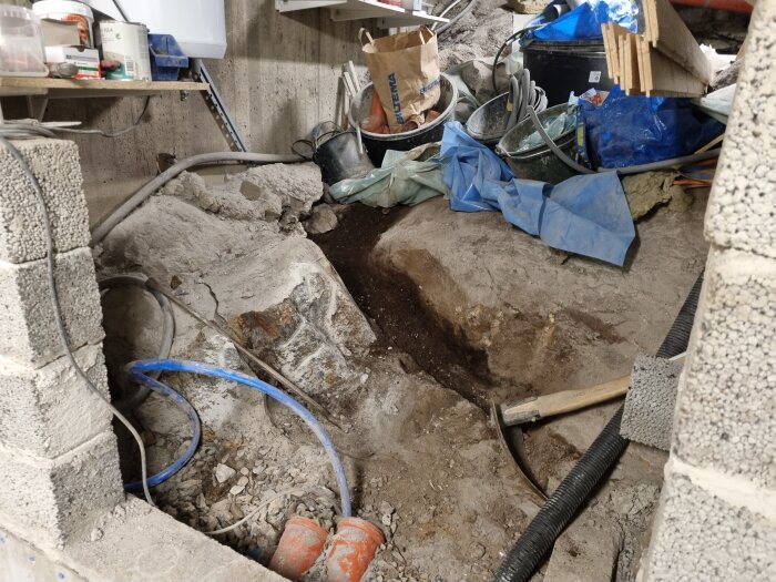 Renoveringsområde inomhus med betongblock, grus, rör och verktyg. Förberedelser för byggprojekt i en bergsskreva.