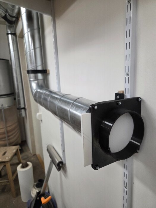 Spånsugssystem med metallrör och väggfästen i ett arbetsrum, del av ett pågående installationsprojekt för dammhantering.