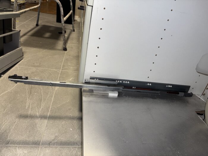 Böjd lådskena under diskbänk i kök, vilket orsakar att lådan hänger snett och slår mot diskmaskinsluckan.