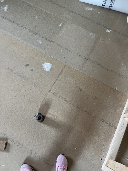 Golv av plywood med ett skadat område och ett rör i rummet under renovering.