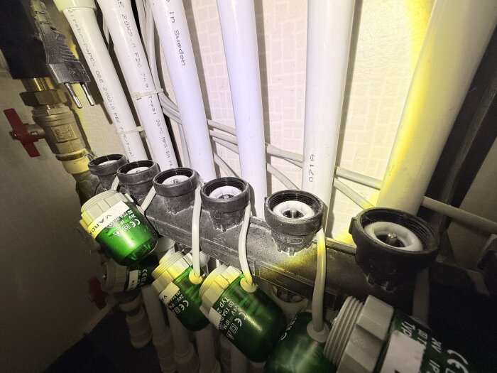 Golvvärmesystem med flera kopplade rör och gröna ventiler, varav en ventil ser ut att sitta lägre än de andra.