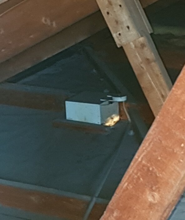 En vit låda på en kallvind, potentiellt kopplad till el, omgiven av träbjälkar och en kabel.
