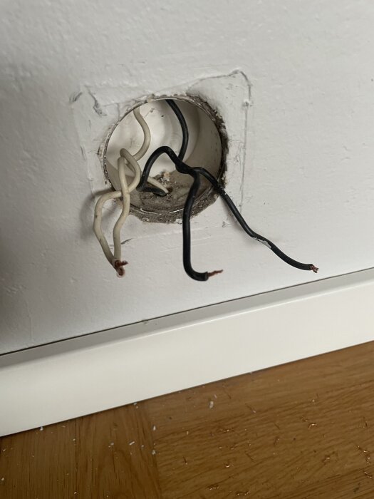 Eluttag med exponerade vita och svarta sladdar i hål i väggen, troligen relaterade till en lampknapp ovanför.