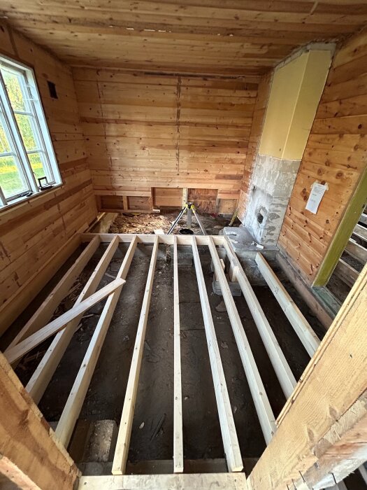 Öppet bjälklag i en renoverad torpargrund med träväggar, delvis synlig jord och nyinstallerade reglar på ett fritidshus.