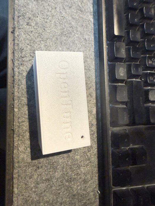 Vit elektroniklåda märkt "OpenTime" bredvid ett tangentbord på en grå matta.
