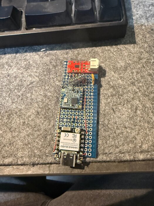 DIY mikrocontrollersystem med Lora sx1262 och andra komponenter på en prototypbräda, liggande på en filtmatta bredvid ett tangentbord.