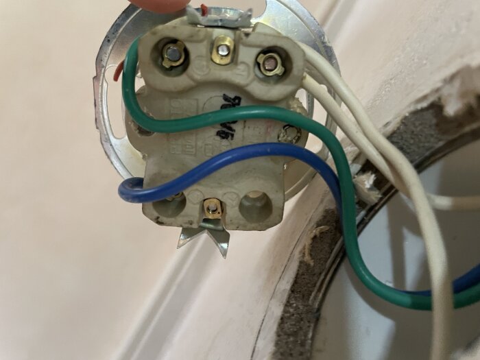 Elektrisk kopplingsdosa med blå och gröna ledningar, monterad i en väggöppning, del av ett pågående installationsarbete.