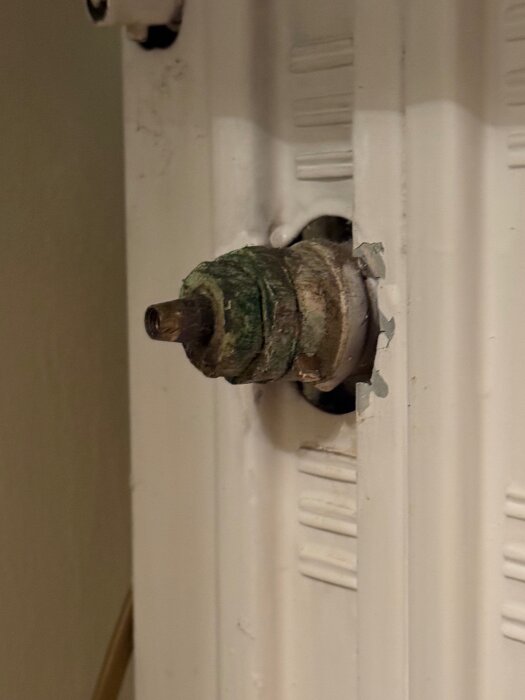 Rostigt och fastärgat ventilvred på vattenburet radiatorrör i ett 50-talshus, omgivande vita elementet och mörka metalldelar synliga.
