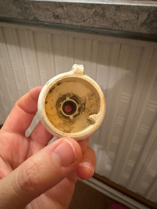 Hand håller ett avtaget vred från en gammal vattenradiator, insidan visar fastärgat metall och smuts.
