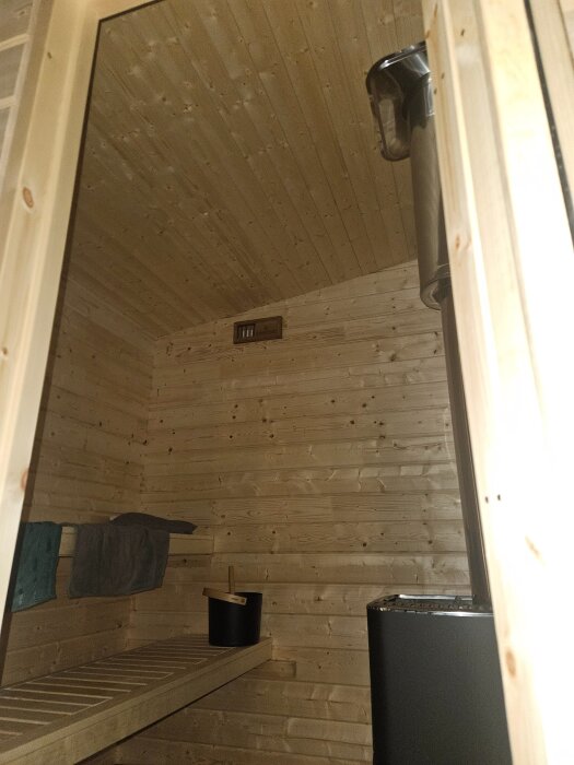 Bastu med lavar, skorsten, ventilationshål och handduk inuti träklädd bastuinteriör, redo för första användningen.