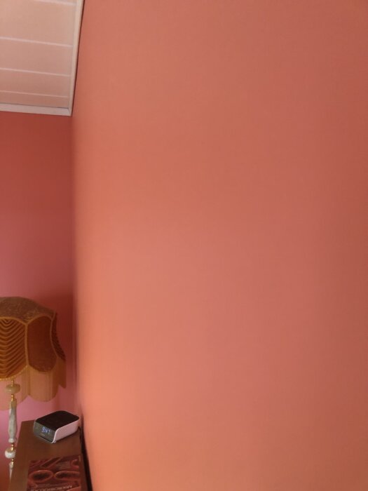 Rosa vägg med slätt resultat efter spackling och målning, en lampskärm och ett bord syns i nederkanten.