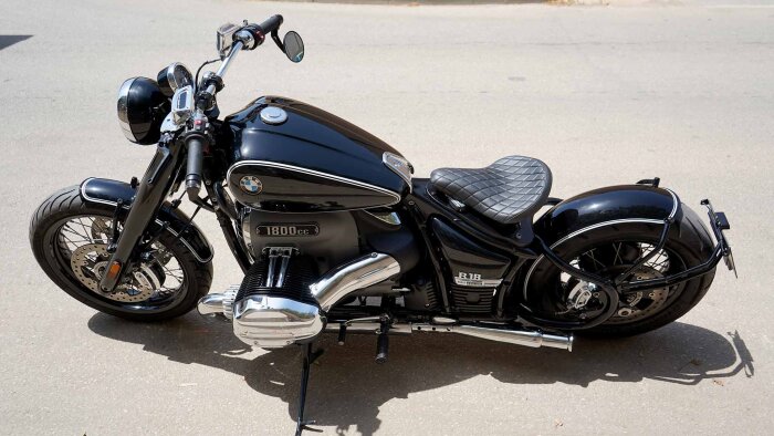 Svart motorcykel BMW R18 med 1800cc-motor och quiltad sadel, fotograferad i soligt väder på asfalt.