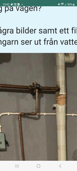 Rörsystem monterat på en vägg med kopparrör och ventiler. Ett av rören är delvis täckt med tejp eller isoleringsmaterial.