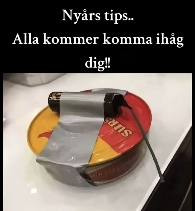 En konservburk med surströmming på ett bord med fyrverkeripjäs fasttejpad på locket, redo för nyårsskämt.
