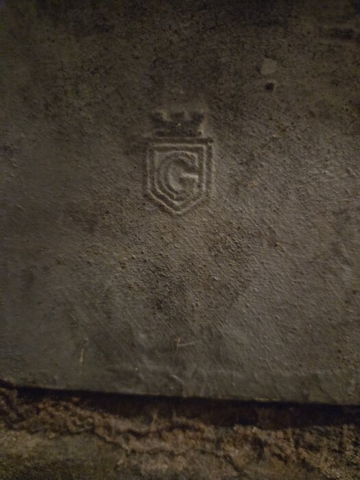 Stenplatta med inristat emblem föreställande en krona och bokstaven "G".