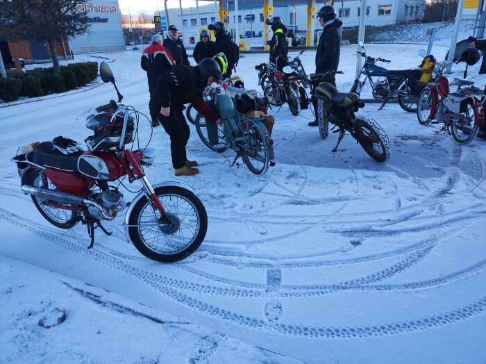 Grupp av människor och mopeder samlade vid en snötäckt väg. Deltagare utrustade med hjälmar förbereder sig för en runda.