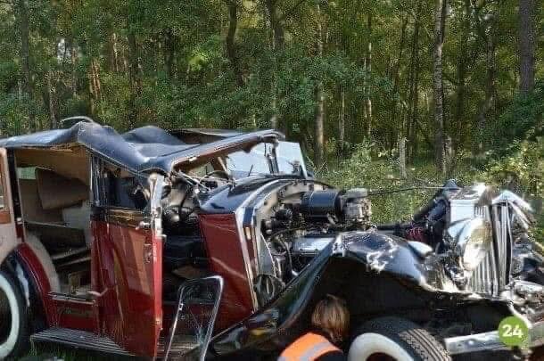 Krockad vintagebil i skogsmiljö, skadad front och öppen dörr.
