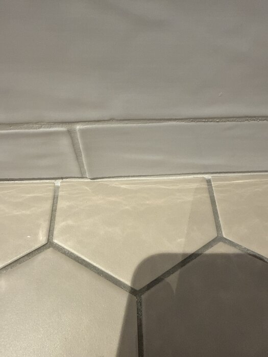 Grå hexagonala klinkers på golv och kvadratiska kakelplattor på väggen.