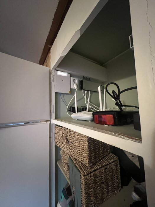 Öppen garderob med teknik- och fiberutrustning på övre hyllan samt flätade korgar och sko på den undre hyllan.