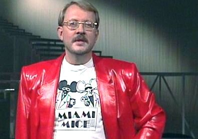 En person i röd jacka och glasögon står i en trappa och bär en t-shirt med texten "MIAMI MICE".