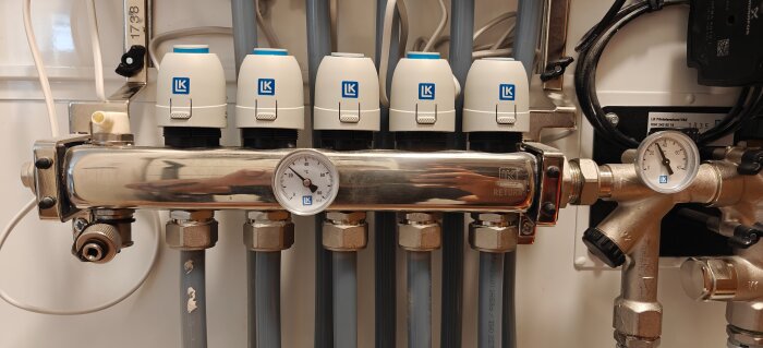LK Systems värmesystem med fem ventiler och två temperaturmätare, anslutet till flera grå rör.
