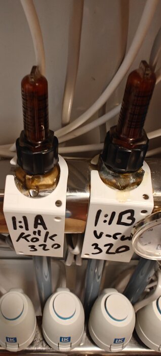 LK Systems värmesystem med märkta flödesmätare och termostater, läckande vatten och kalkavlagringar synliga vid anslutningarna.