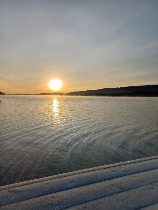 Solnedgång över vatten vid Mjältön, Höga kusten, en stilla kväll med klar himmel och solreflektion på vattnet.