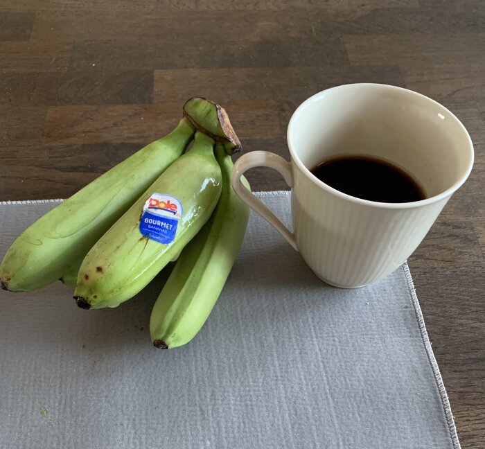 Gröna bananer med klistermärken och en kopp kaffe på ett bord.