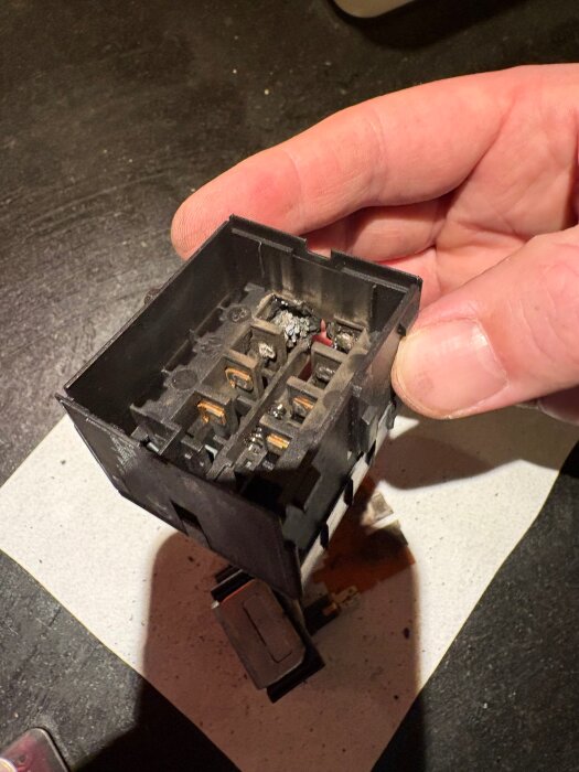 Närbild på en elektrisk kontaktor med brända markeringar och skador, håller i en hand.