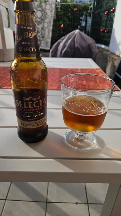 Flaska och glas med San Miguel Selecta öl på ett vitt bord utomhus.