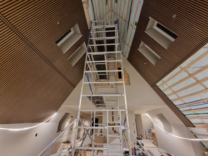 Byggplats på gott nytt år med stege uppställd inomhus, omgiven av nyinstallerad köksbelysning med träpanel på väggarna.