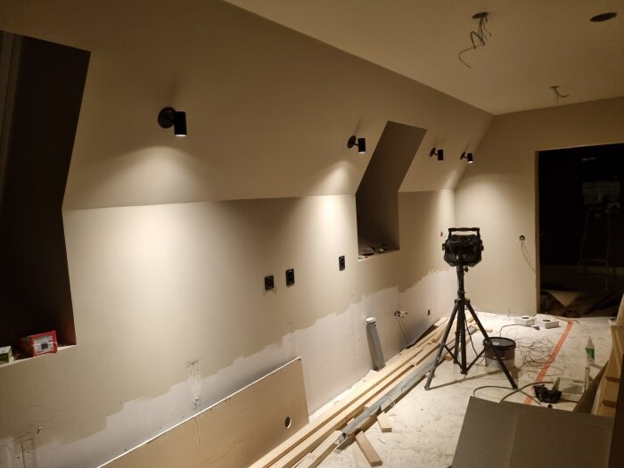 Nytt köksbygge med nyinstallerade spotlights på väggen, en arbetslampa och verktyg utspridda på golvet.