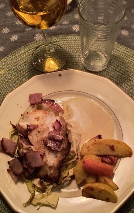 Torskrygg med bräckt skinka och champagnesås på ugnsbakad spetskål, serverad med potatisklyftor och morot på en tallrik.