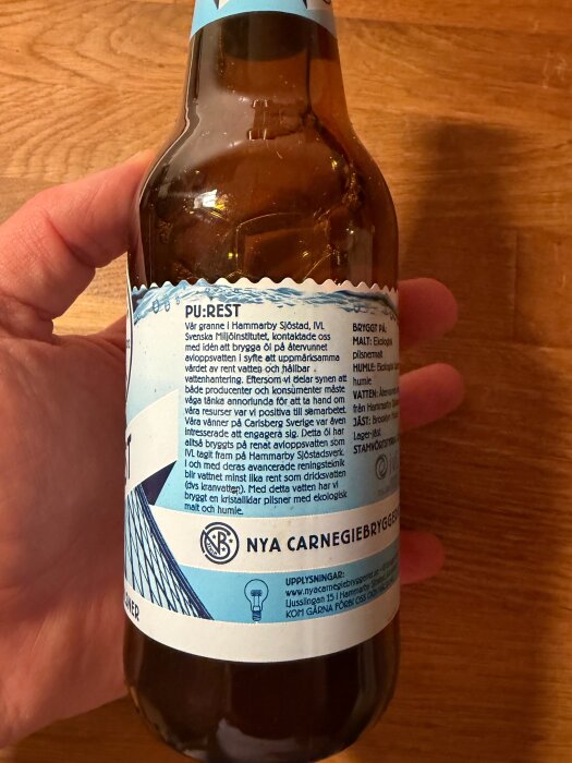 Närbild på en ölflaska från Nya Carnegiebryggeriet med etiketttext om tillverkning av öl med återvunnet vatten, hållbart bryggeriinitiativ.