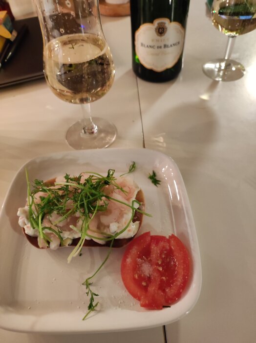 Skagentoast serverad på jollekaka med tomatklyfta och dill, bredvid glas och flaska av Blanc de Blancs.