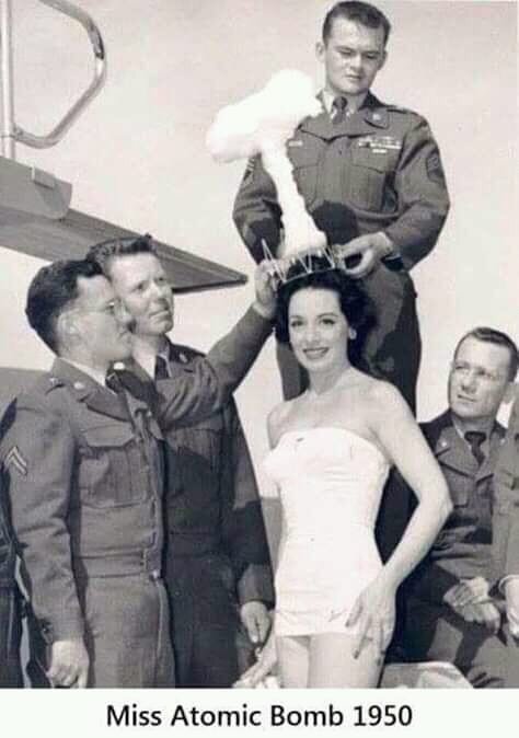 Kvinna i baddräkt kröns med tiara formad som ett svampmoln omgiven av fyra män i militäruniformer. Texten "Miss Atomic Bomb 1950" syns nedtill.
