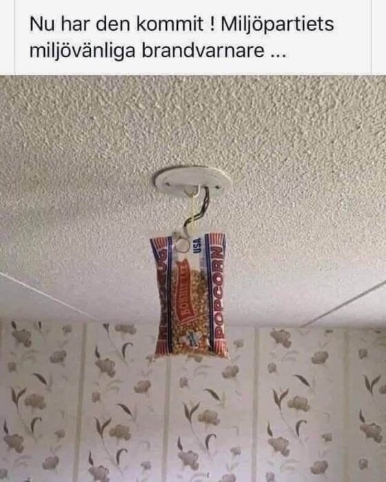En påse popcorn hängande från taket, monterad där en brandvarnare vanligtvis sitter, med text som skämtar om en miljövänlig brandvarnare.