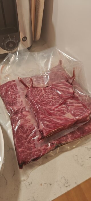 Vakuumförpackade köttbitar ligger på en köksbänk bredvid en hushållsmaskin.