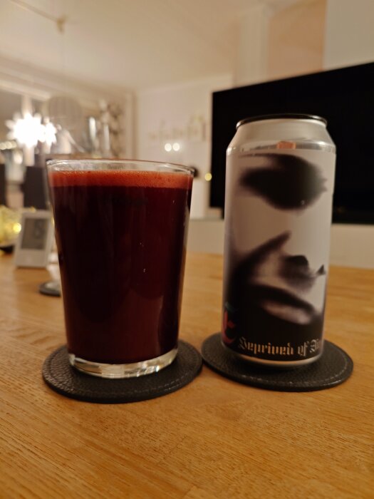 Glas med mörkröd syrlig öl bredvid en burk med konstnärlig etikett på ett träbord, inomhus med mjuk belysning.