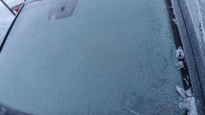 Frostig bilruta med snökanter efter att ha skrapats; is kvar på kanten.
