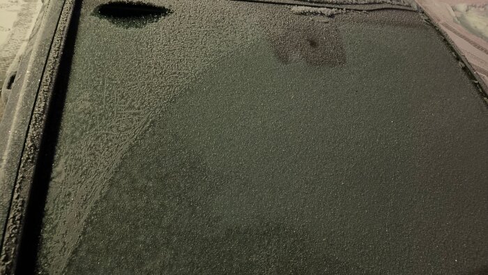 Frostig bilruta med delvis smält frost, visar arbete med att skrapa och värma upp för bättre sikt.