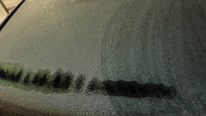 Nedfrostad ruta där is delvis skrapats bort, visar processen efter tomgångskörning för avfrostning.